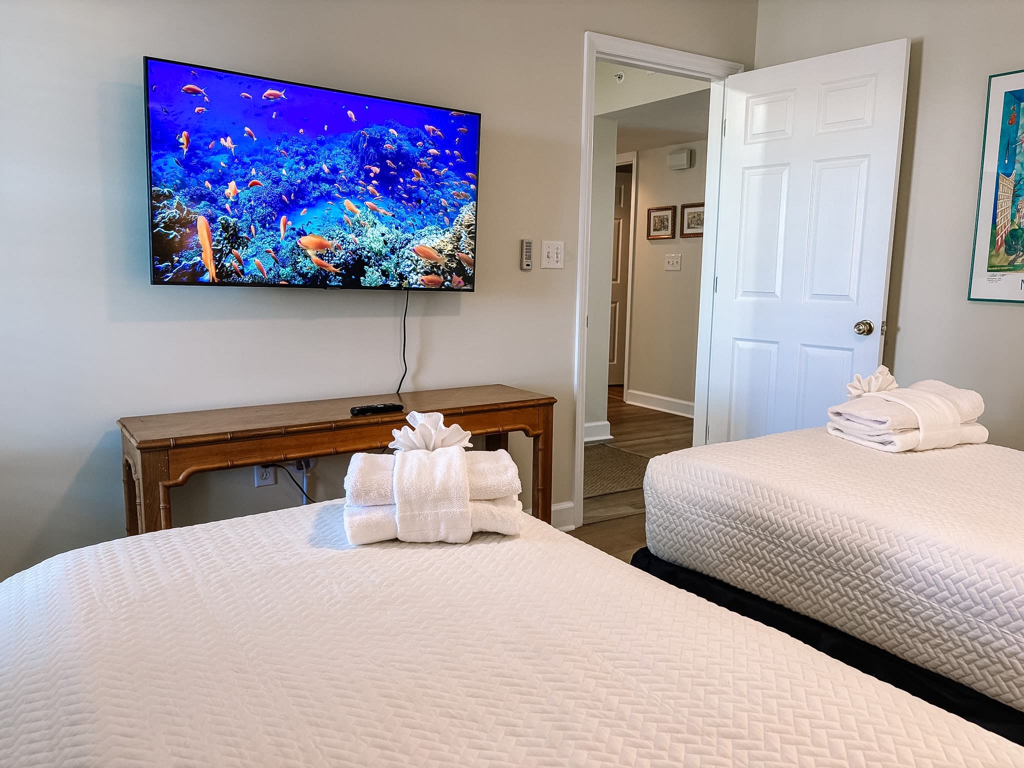 Bedroom featuring two white beds and a wall-mounted TV displaying a colorful underwater scene.