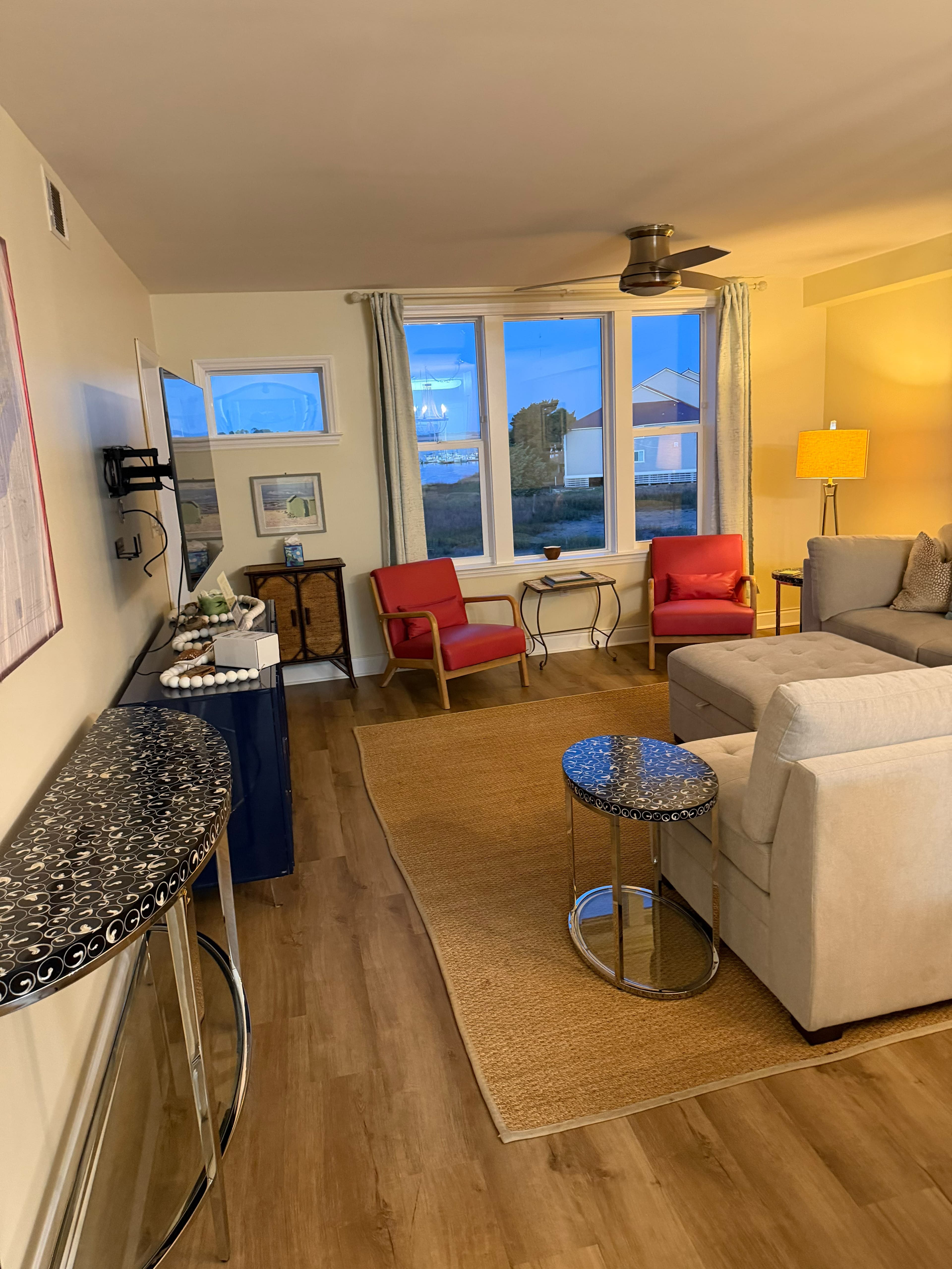 Modern living room with red armchairs, grey sectional, and large windows overlooking a coastal view.